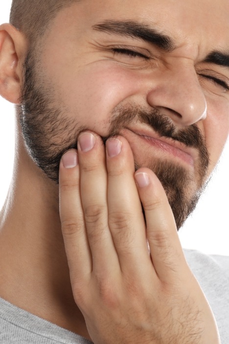 Man holding cheek in pain and needing emergency dentist in Millis