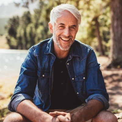 Older man sitting on log with pond in background