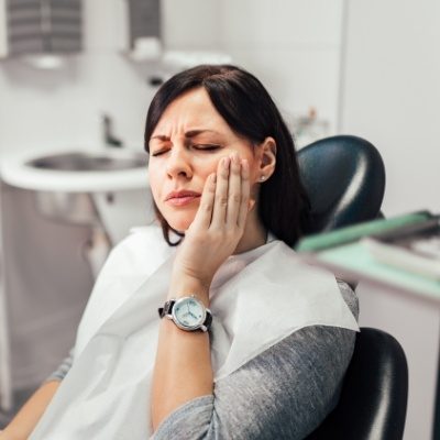 Woman in dental chair holding her cheek in pain