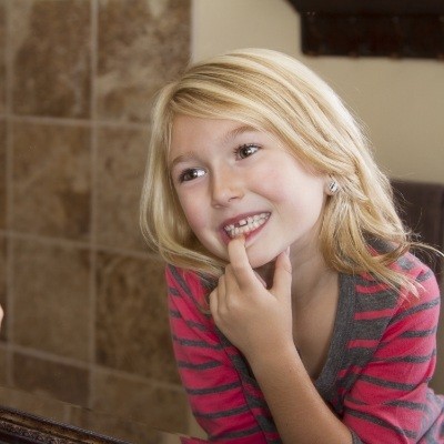 Young girl looking at her tooth in a mirror