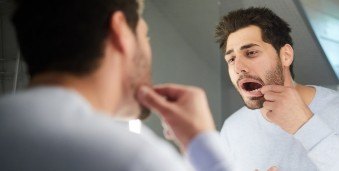 Man looking at his gums in bathroom mirror